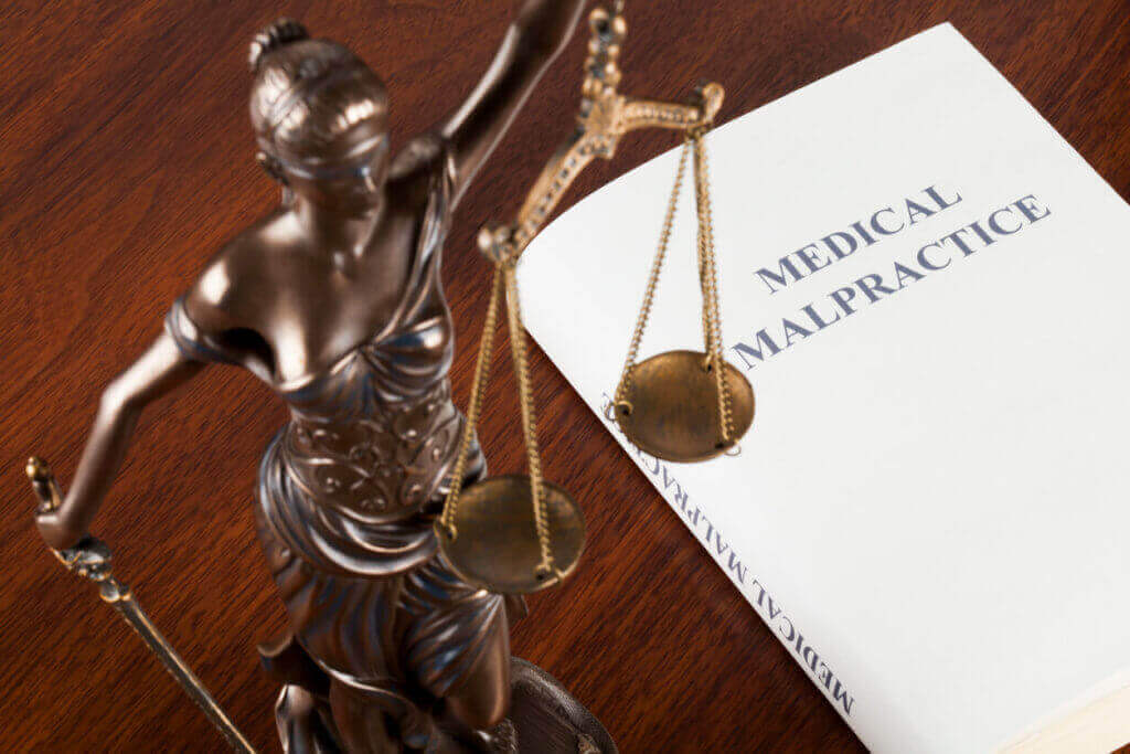 Lady Justice statue with scales next to a book titled "Medical Malpractice" on a wooden table.